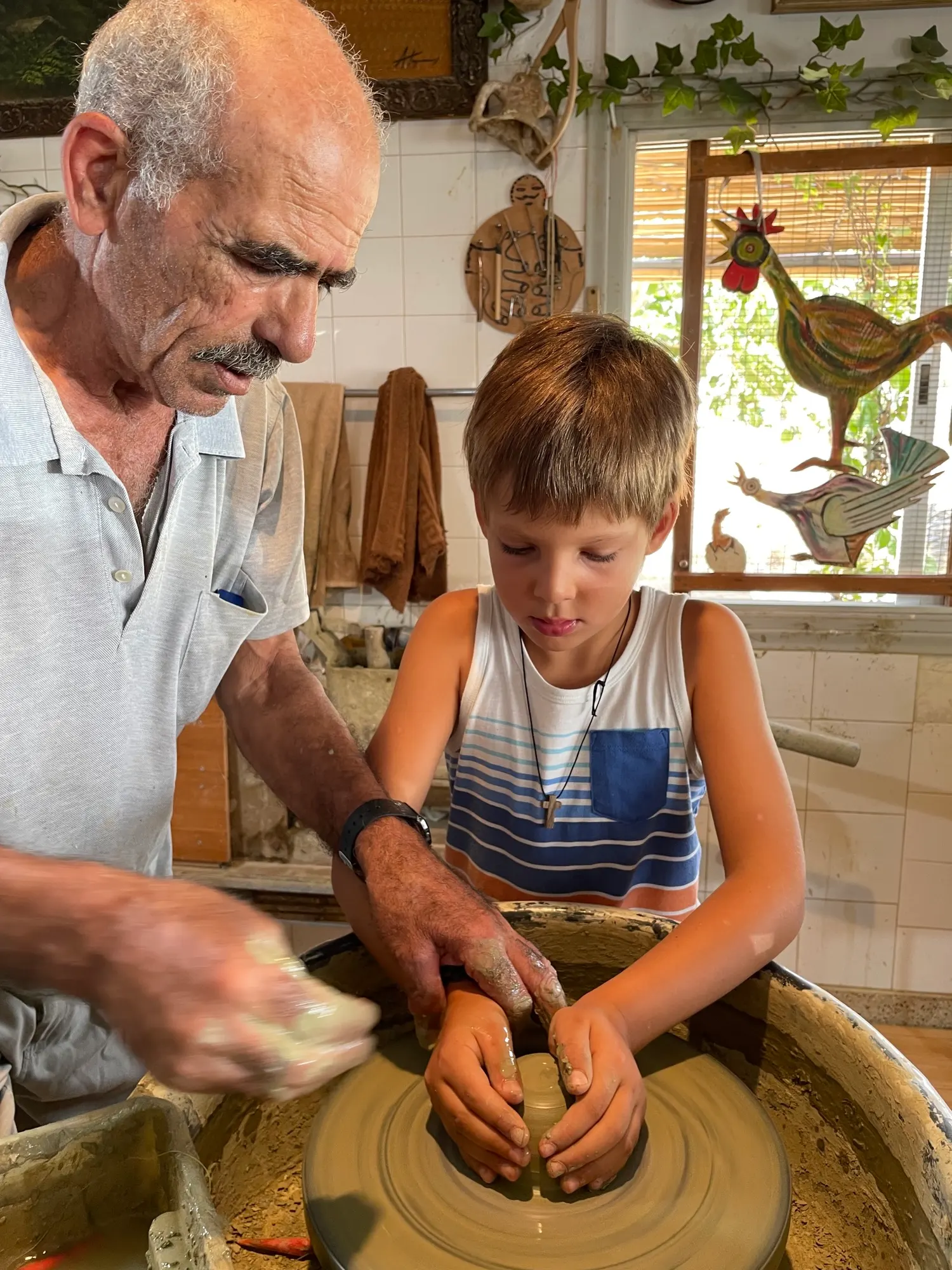 Volunteer helps child make clay cup on wheel